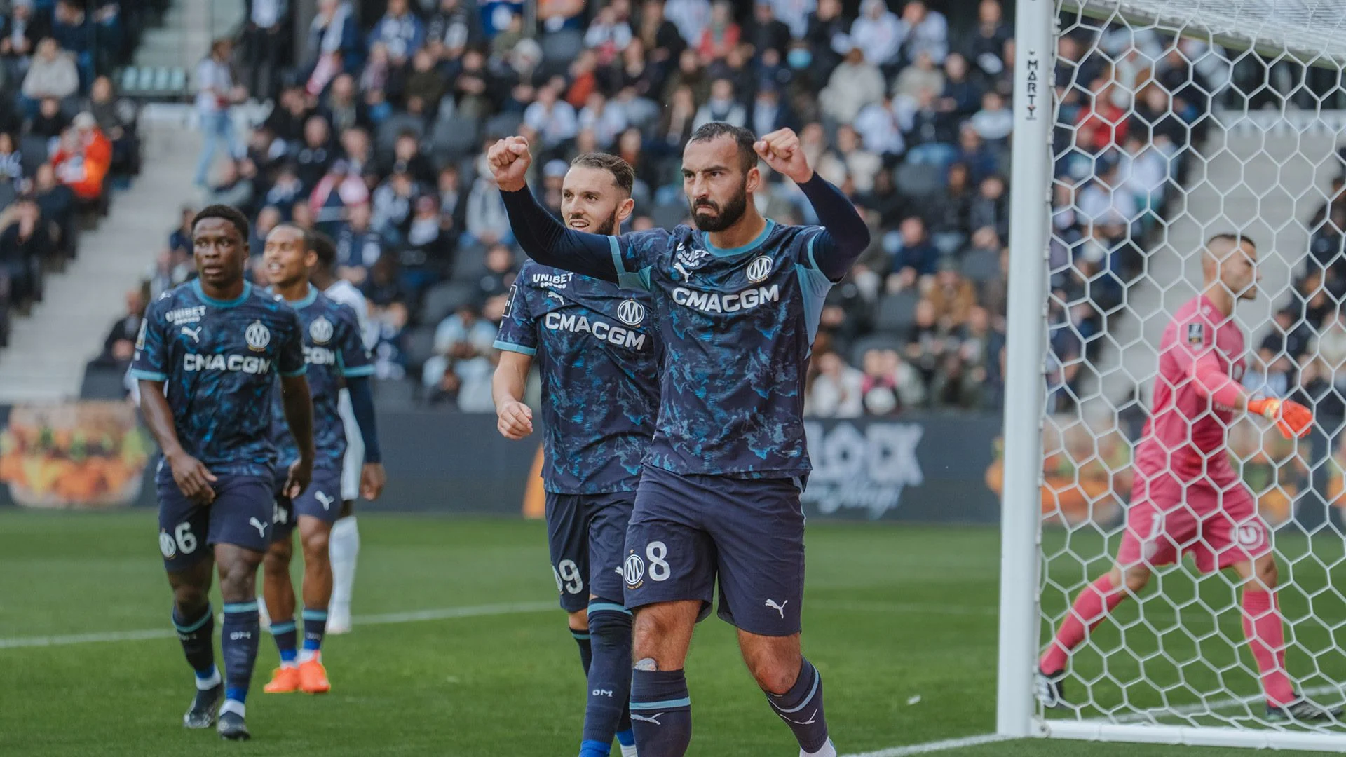 Marseille midfielder Himad Abdelli, wearing No 8 in the club's navy kit, clenches both fists in celebration with team-mates beside the Angers goal at the Stade Raymond-Kopa, as Angers goalkeeper Anthony Lopes stands in pink at right. Photo: Olympique de Marseille