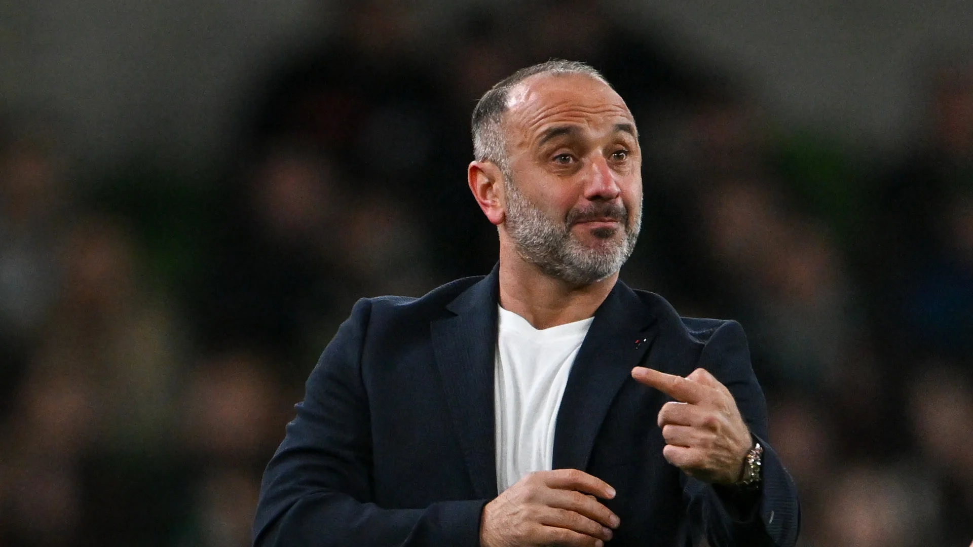 Armenia head coach Yeghishe Melikyan in a dark blazer and white T-shirt gesturing on the touchline