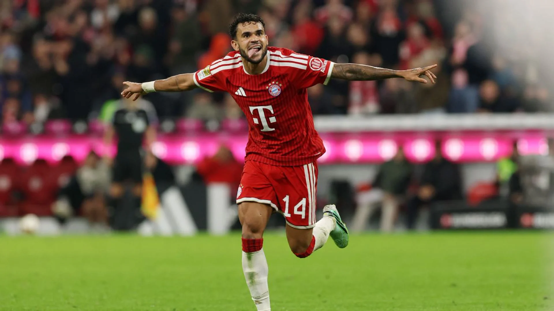 Luis Díaz, wearing No 14 in Bayern Munich's red home kit, celebrates with his arms outstretched during the 6-1 Bundesliga win over RB Leipzig at the Allianz Arena, with the crowd and pitchside boards behind him. Photo: Alexander Hassenstein/Getty Images