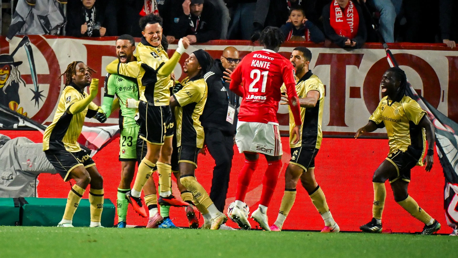 OGC Nice players in their gold away kit celebrate around goalkeeper Yéhvann Diouf, in green, late in the match at the Stade Francis-Le Blé, as Brest's Ibrahim Kanté walks past in red. Photo: OGC Nice