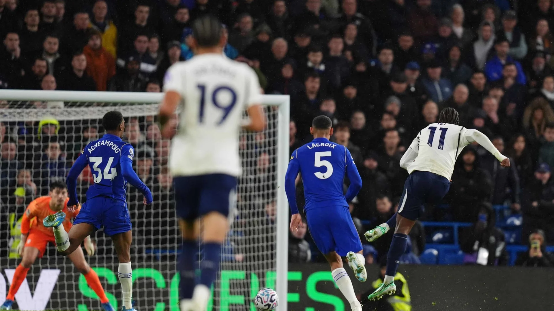 Tottenham forward Mathys Tel (No 11), in Tottenham's white shirt, shoots for his 87th-minute goal as Chelsea defenders Josh Acheampong (No 34) and Maxence Lacroix (No 5) chase and goalkeeper Mike Penders sets himself, at a rainy Stamford Bridge on 24 October 2026. Photo: John Walton/PA