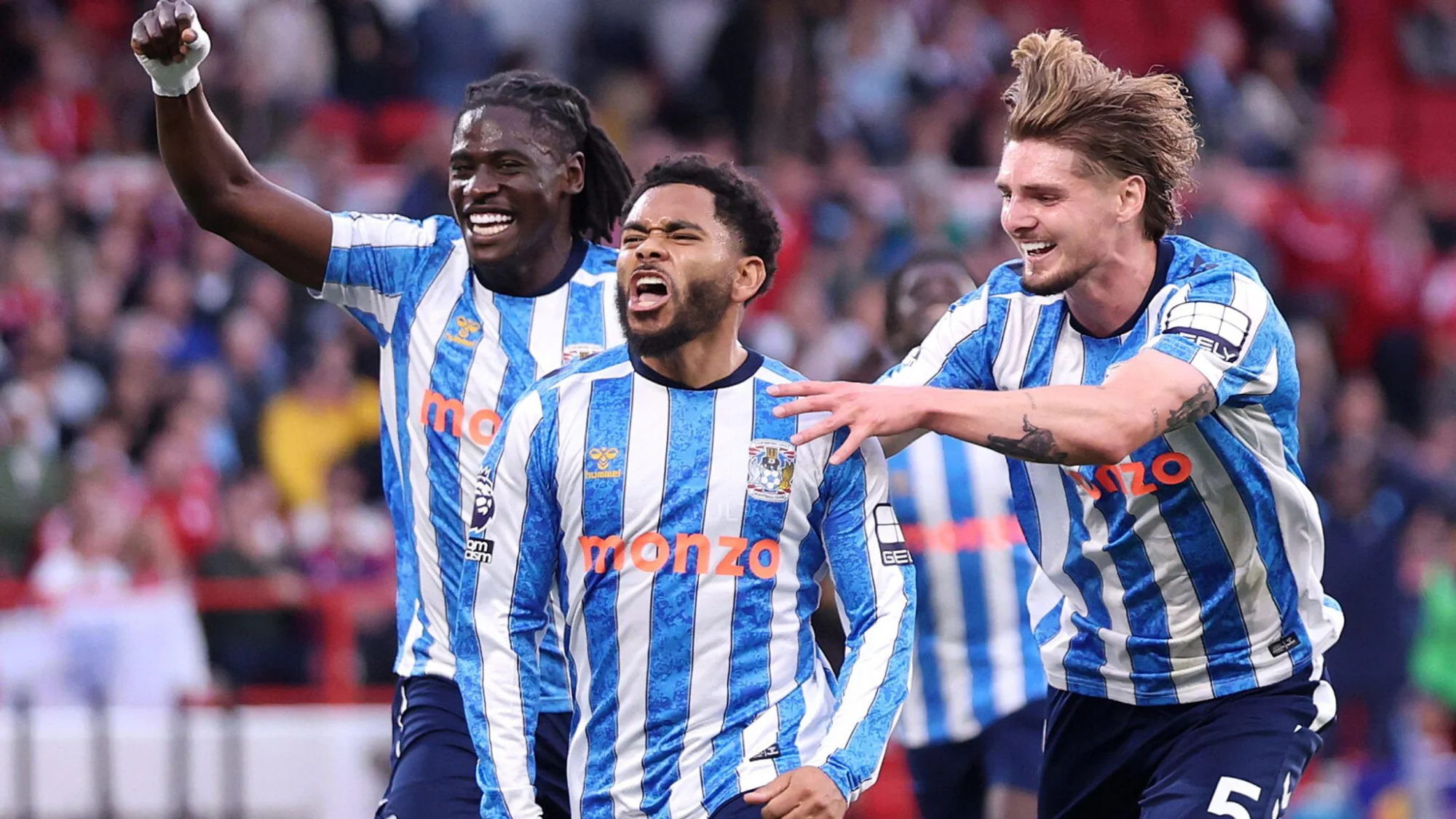 Coventry City players in blue-and-white striped kits celebrate a goal together in front of a stadium crowd. Photo: Sky Sports
