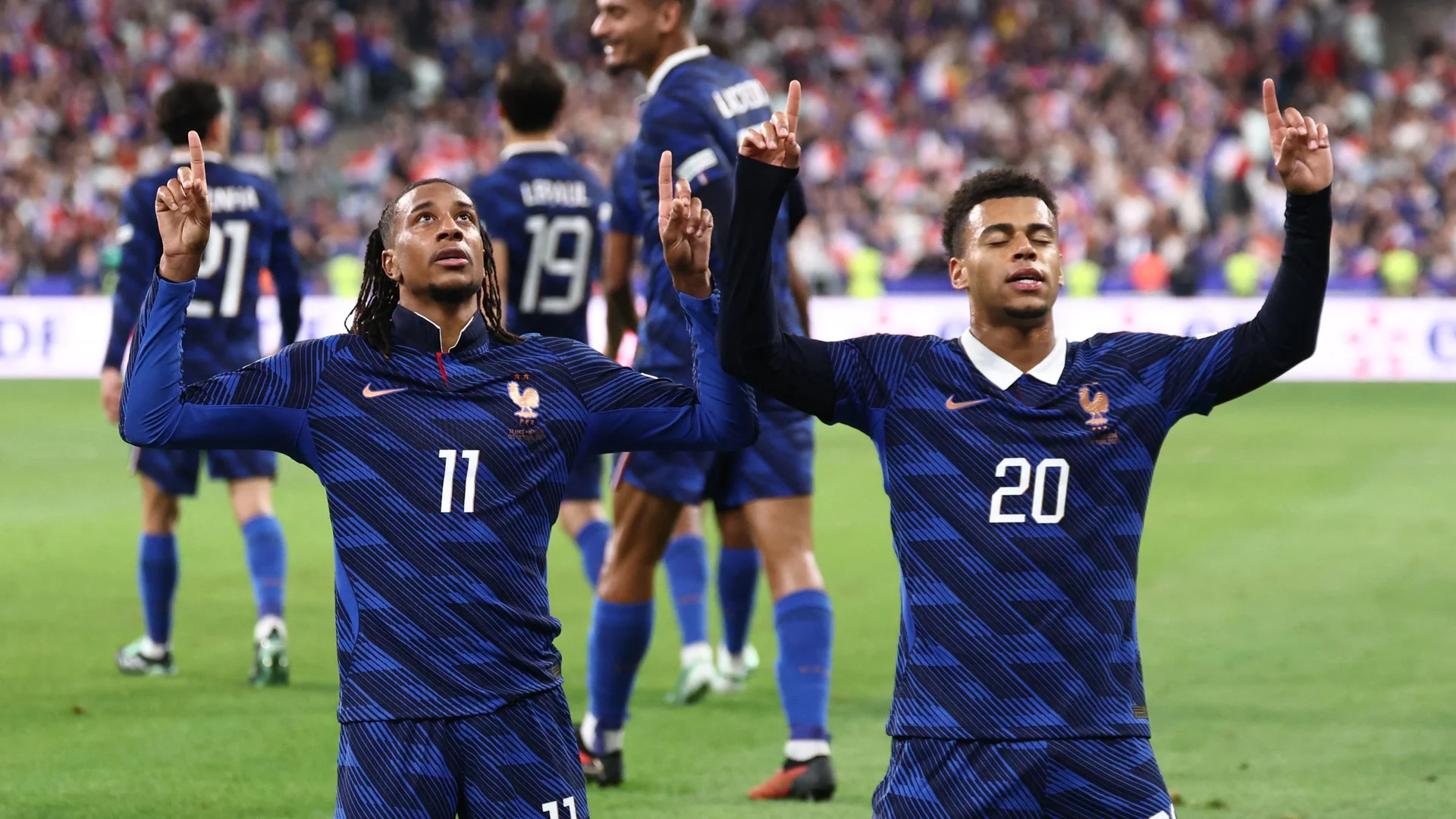 Michael Olise (No 11) and Désiré Doué (No 20) kneel and point to the sky in France's blue national-team shirts after a goal against Belgium at the Stade de France (Photo: AFP via Getty Images)