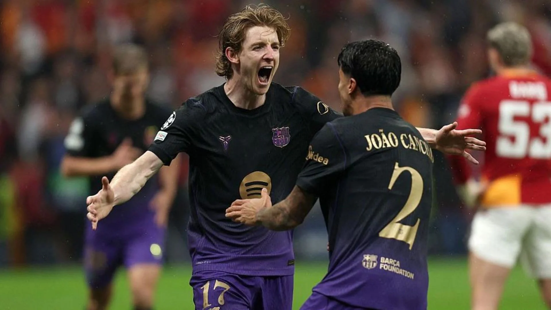 Anthony Gordon in Barcelona's dark away kit celebrates with arms wide beside João Cancelo after a Champions League goal at RAMS Park, with a Galatasaray player in red and orange nearby. Photo: BBC Sport / Getty Images