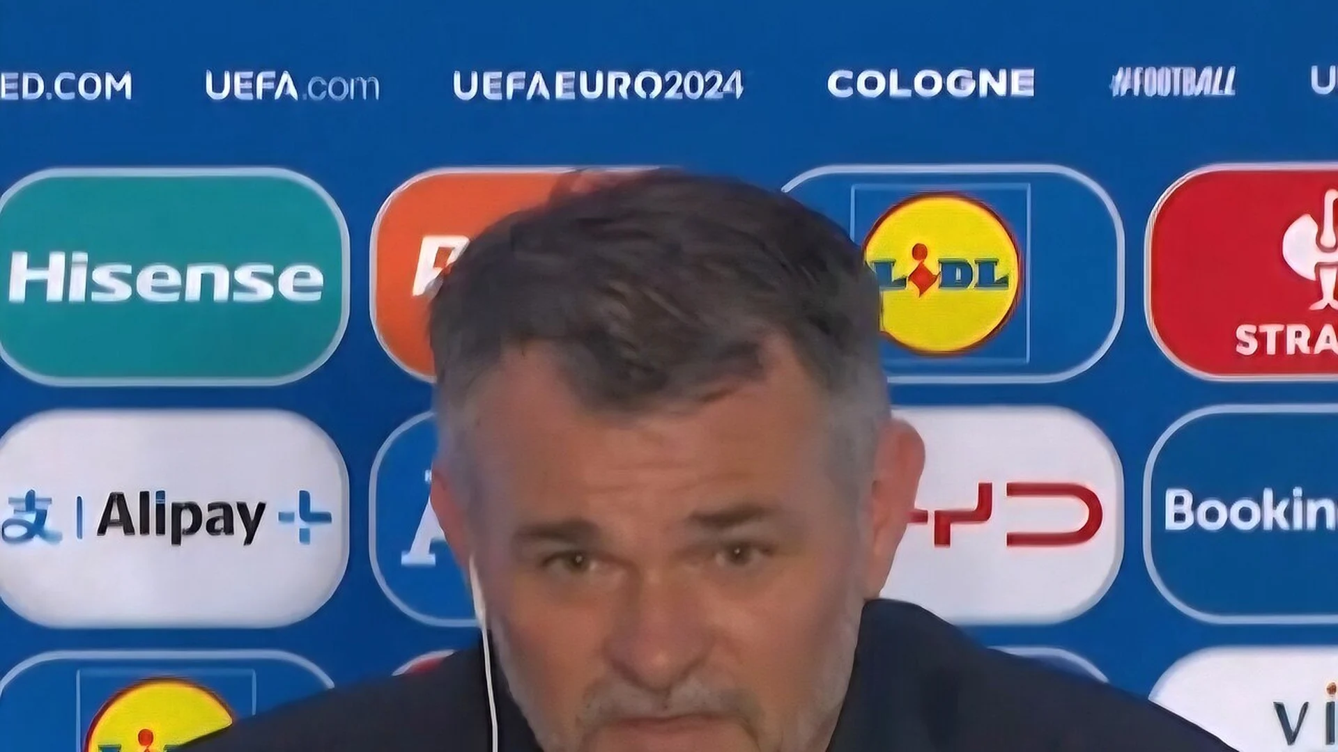 Willy Sagnol in a dark jacket at a UEFA Euro 2024 press conference in Cologne with tournament backdrop