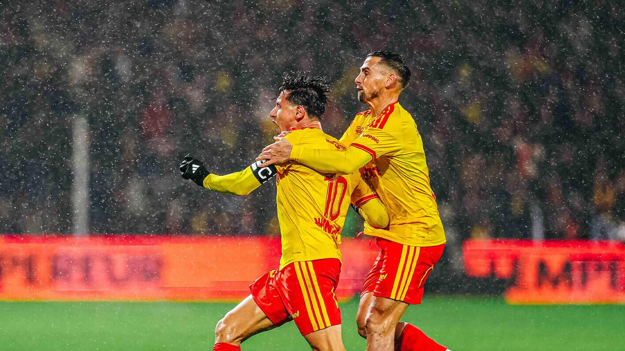 Lens captain Florian Thauvin, wearing the No 10 yellow shirt and red shorts with the captain's armband, celebrates with his arm raised as a team-mate embraces him from behind in heavy rain at the Stade Bollaert-Delelis on 24 October 2026. Photo: RC Lens