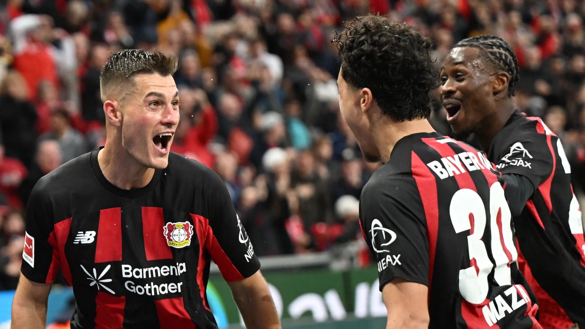Patrik Schick, in Bayer Leverkusen's red and black home kit, celebrates his winning goal against SC Freiburg at the BayArena with Ibrahim Maza (No 30) and Nathan Tella. Photo: Ina Fassbender via Bundesliga.com