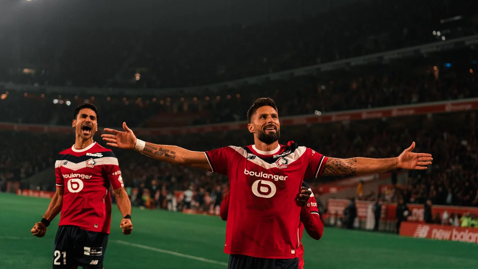 Olivier Giroud celebrates with arms outstretched in Lille's red home kit during the derby win over Lens at Stade Pierre-Mauroy