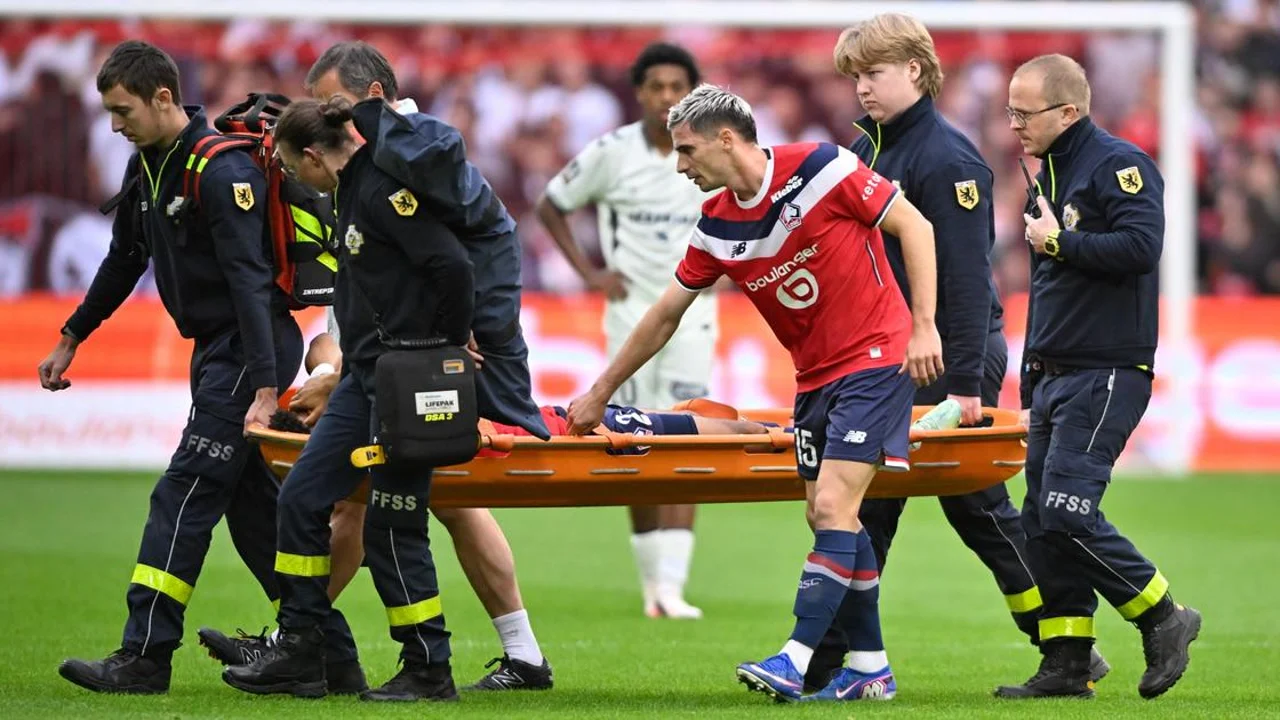 Tiago Santos is carried off on a stretcher by medical staff at Stade Pierre-Mauroy as a Lille team-mate in the red home shirt walks alongside during Lille v Le Havre. Photo: Le Figaro / AFP