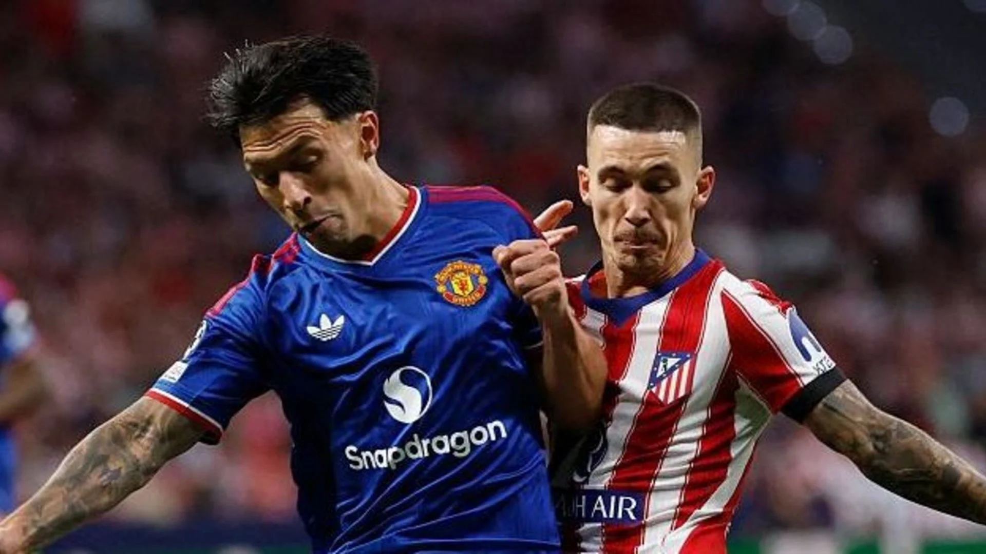 Lisandro Martínez in Manchester United's blue away kit battles an Atlético Madrid player in red-and-white stripes during the Champions League match in Madrid.