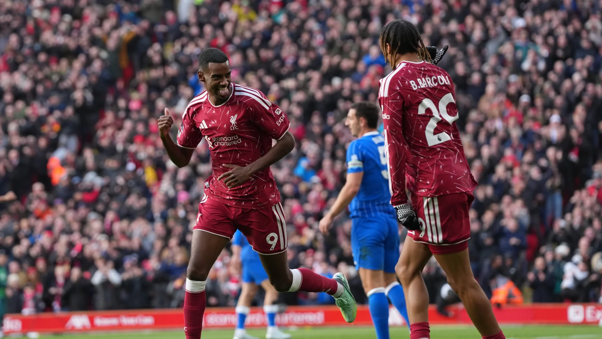 Liverpool striker Alexander Isak, in Liverpool's red home shirt with the No 9 on his shorts, smiles and gives a thumbs-up as he celebrates his goal against Brighton & Hove Albion at Anfield on 25 October 2026, with team-mate Bradley Barcola (No 29) beside him and a Brighton player in blue behind. Photo: Liverpool FC
