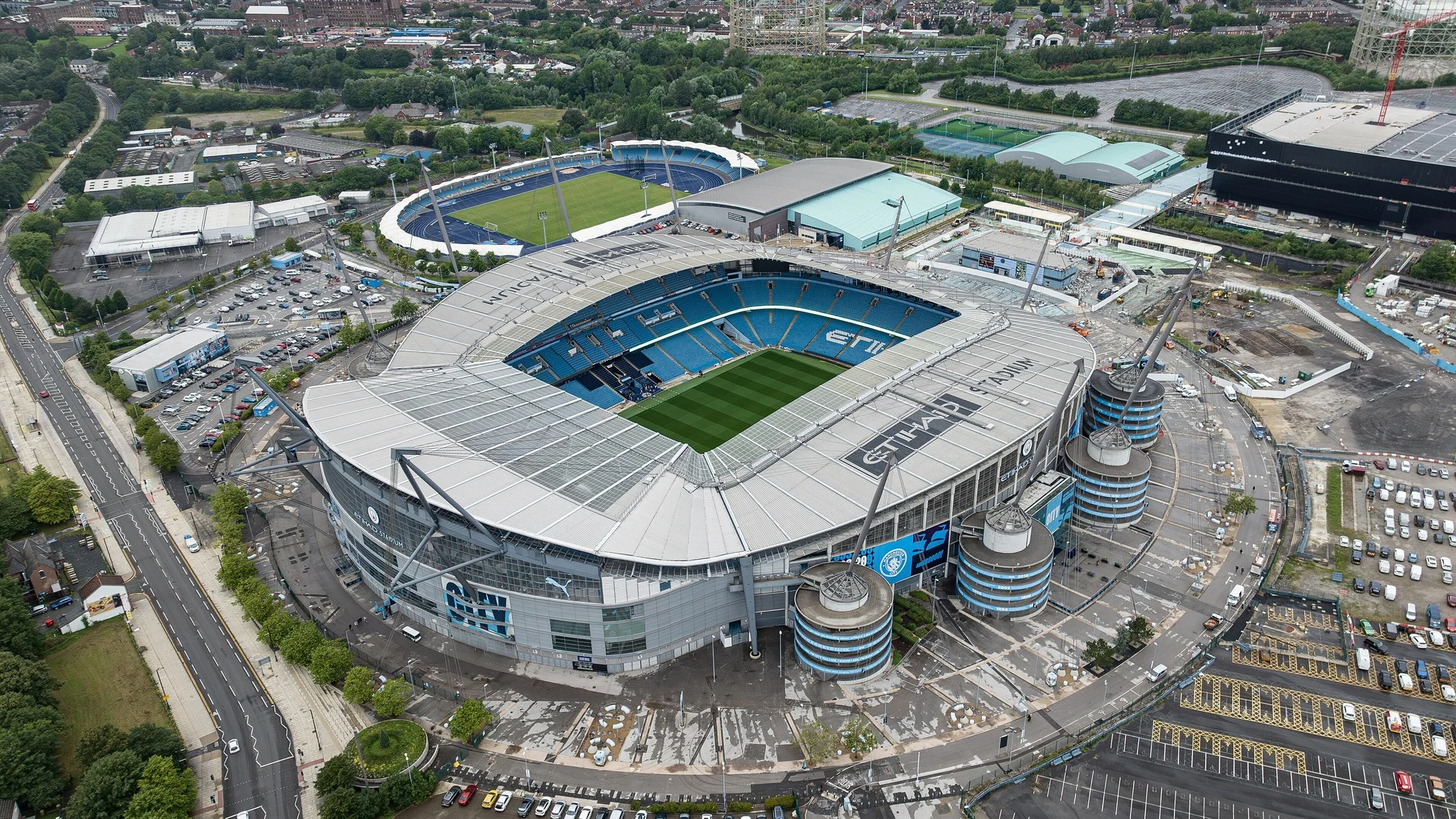 Aerial view of Manchester City’s Etihad Stadium with the pitch and roof masts visible on an overcast day