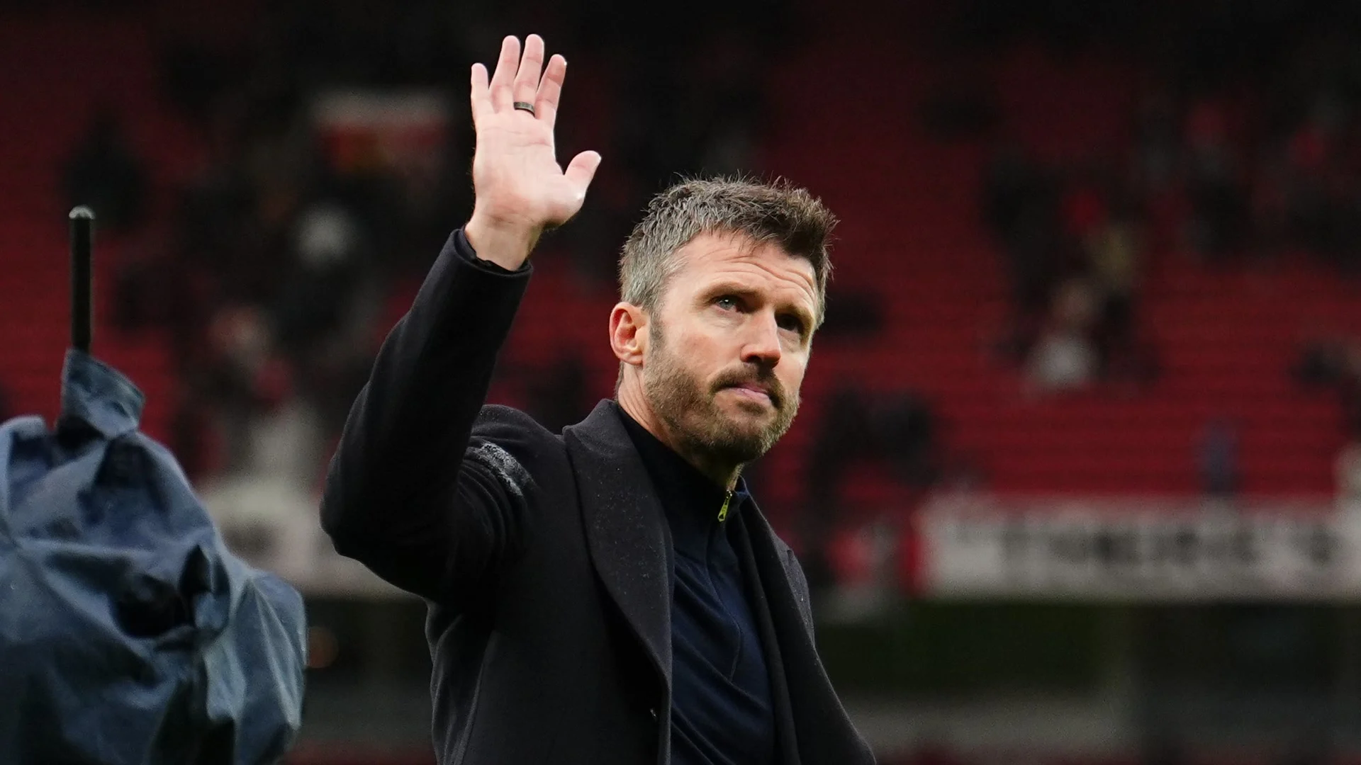 Manchester United head coach Michael Carrick, in a dark overcoat, raises his hand to wave to supporters at Old Trafford. Photo via The Independent