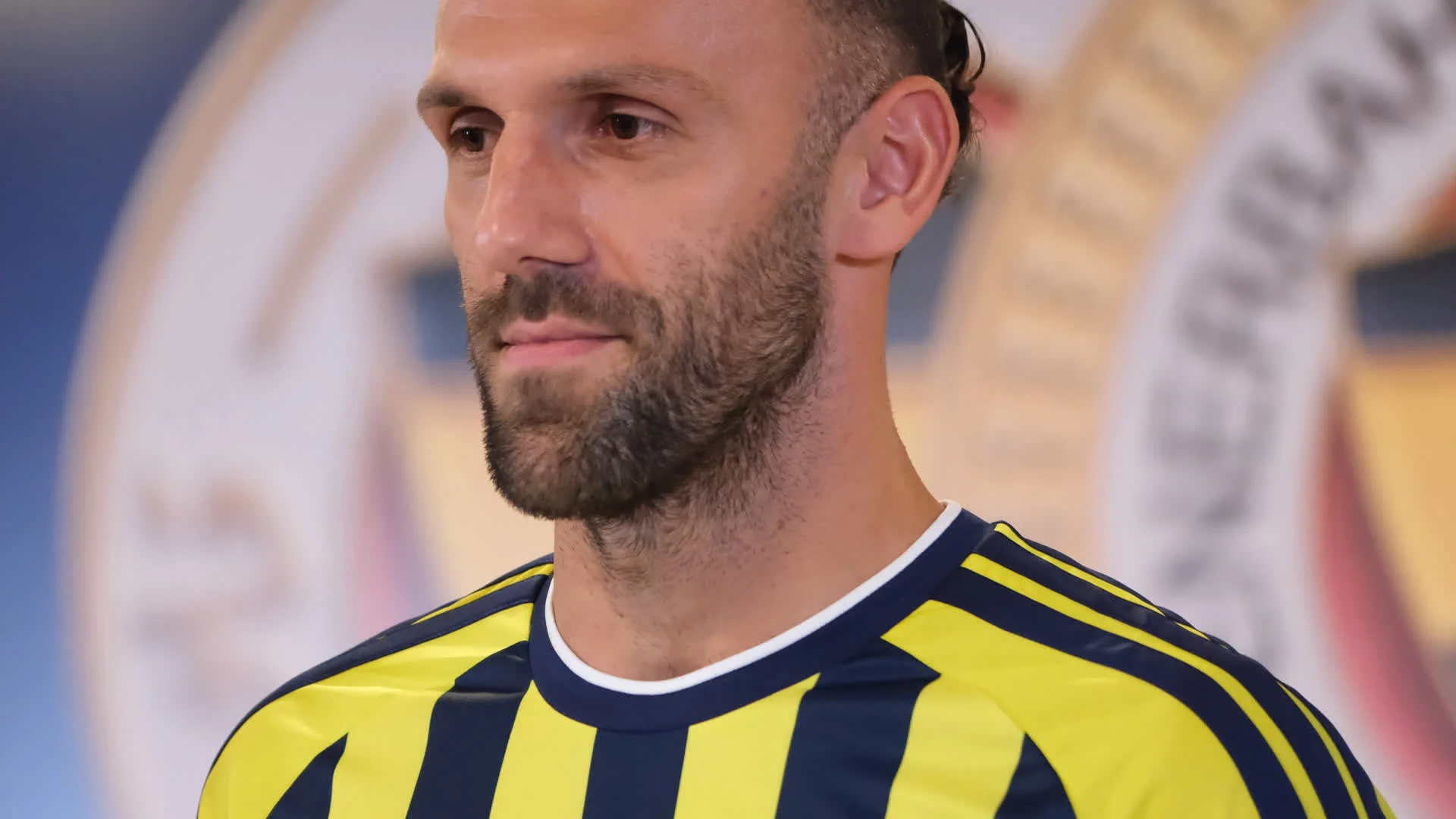 Vedat Muriqi in a Fenerbahçe striped jersey looking down during a media appearance in July 2026
