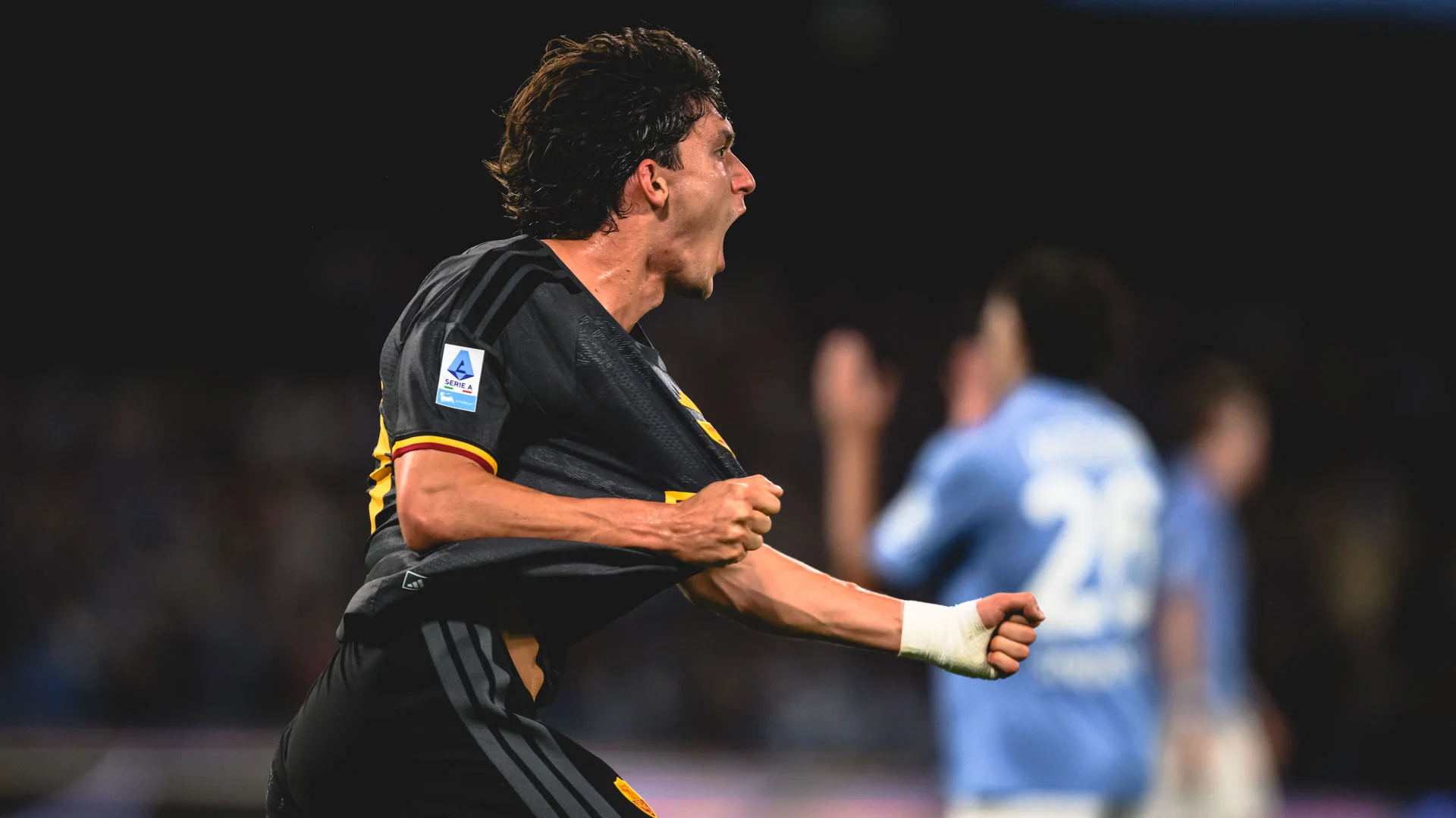 Roma defender Leonardo Balerdi, in Roma's black away kit, celebrates one of his two goals with a shout and clenched fists as blurred Napoli players in light blue stand behind him at the Stadio Diego Armando Maradona on 24 October 2026. Photo: AS Roma