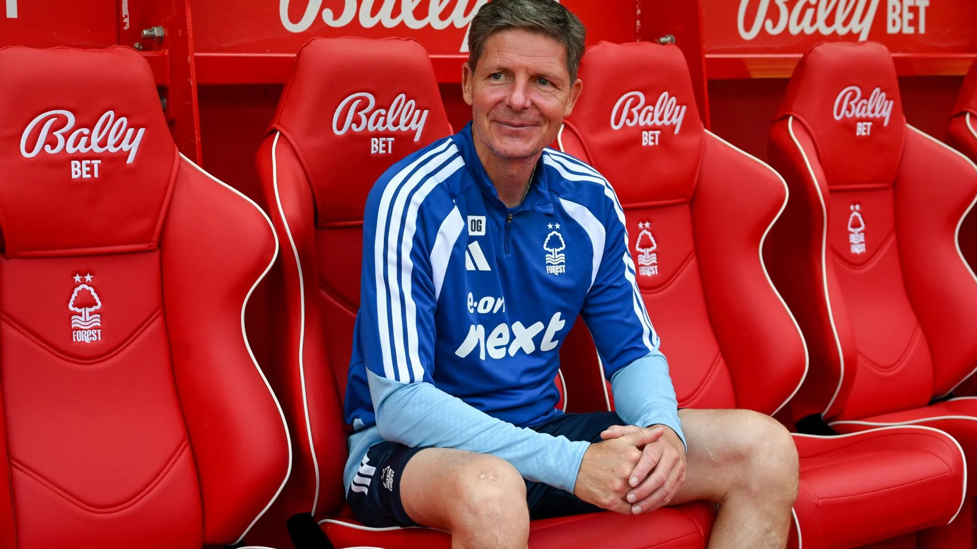 Oliver Glasner smiling in a blue Nottingham Forest training top in the dugout