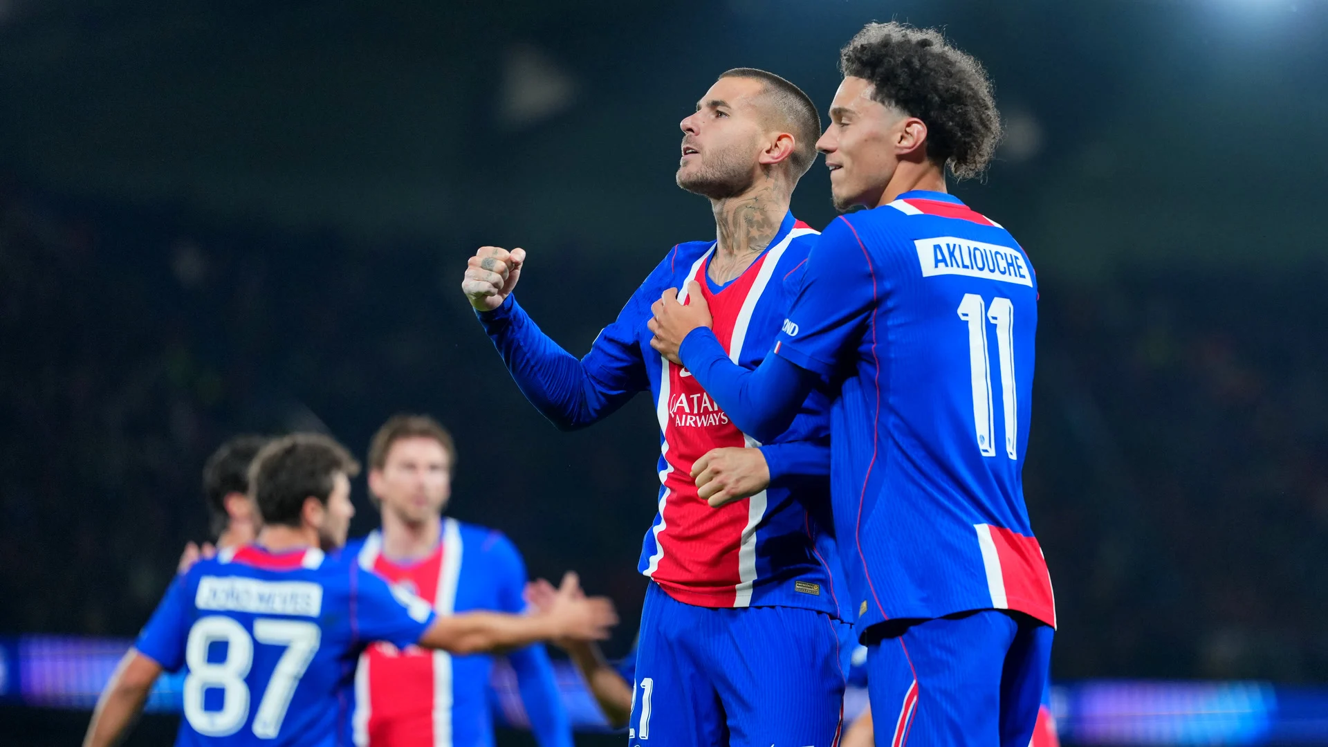 Lucas Hernández, in Paris Saint-Germain's blue and red home kit, clenches his fist as he celebrates his headed goal against Barcelona with Maghnes Akliouche (number 11) at the Parc des Princes, with João Neves (number 87) and teammates behind. Photo: Franco Arland/Getty Images