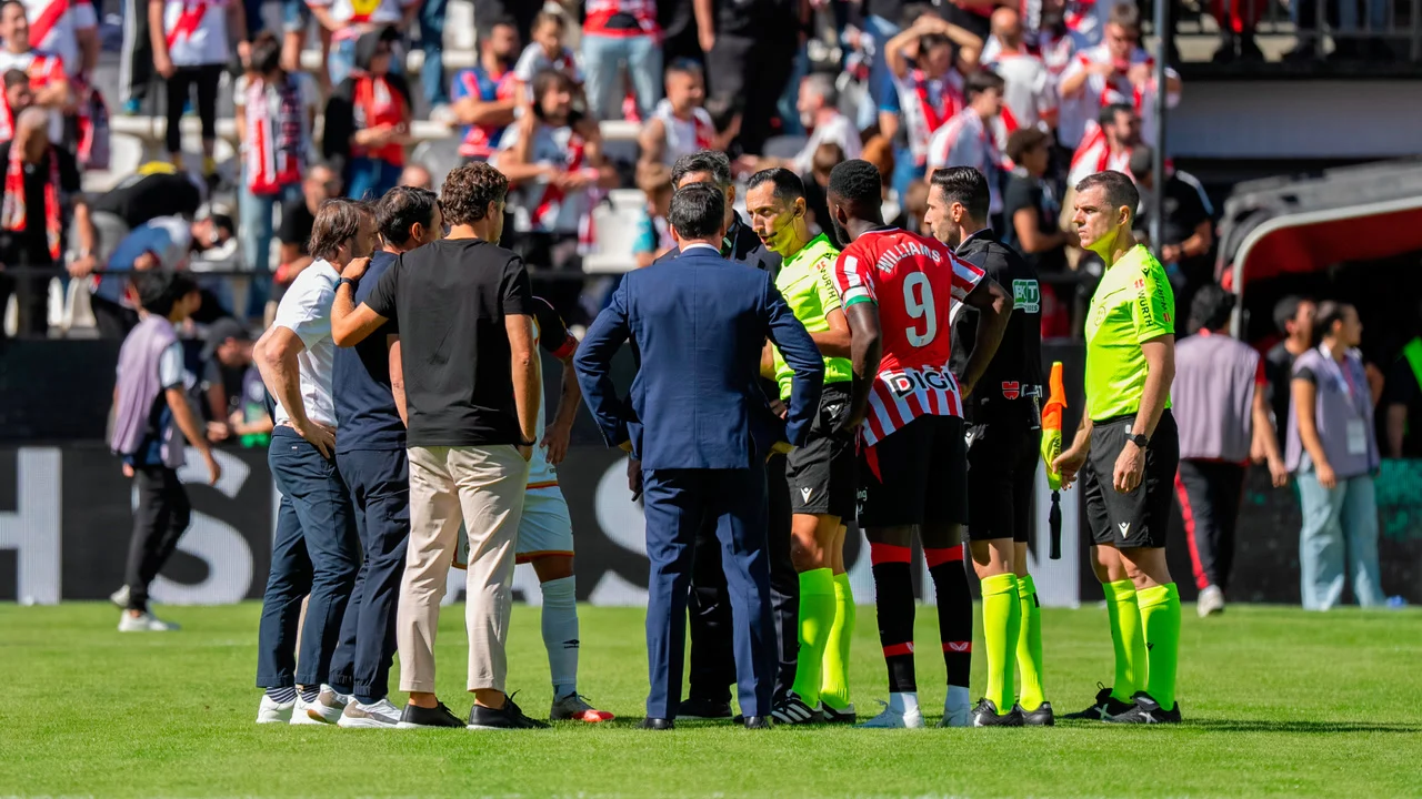 Referee José María Sánchez Martínez speaks with the coaches and captains, including Athletic Club's Iñaki Williams in the red-and-white striped kit, before the Rayo Vallecano game is called off at the Estadio de Vallecas. Photo: Pablo Moreno/Marca