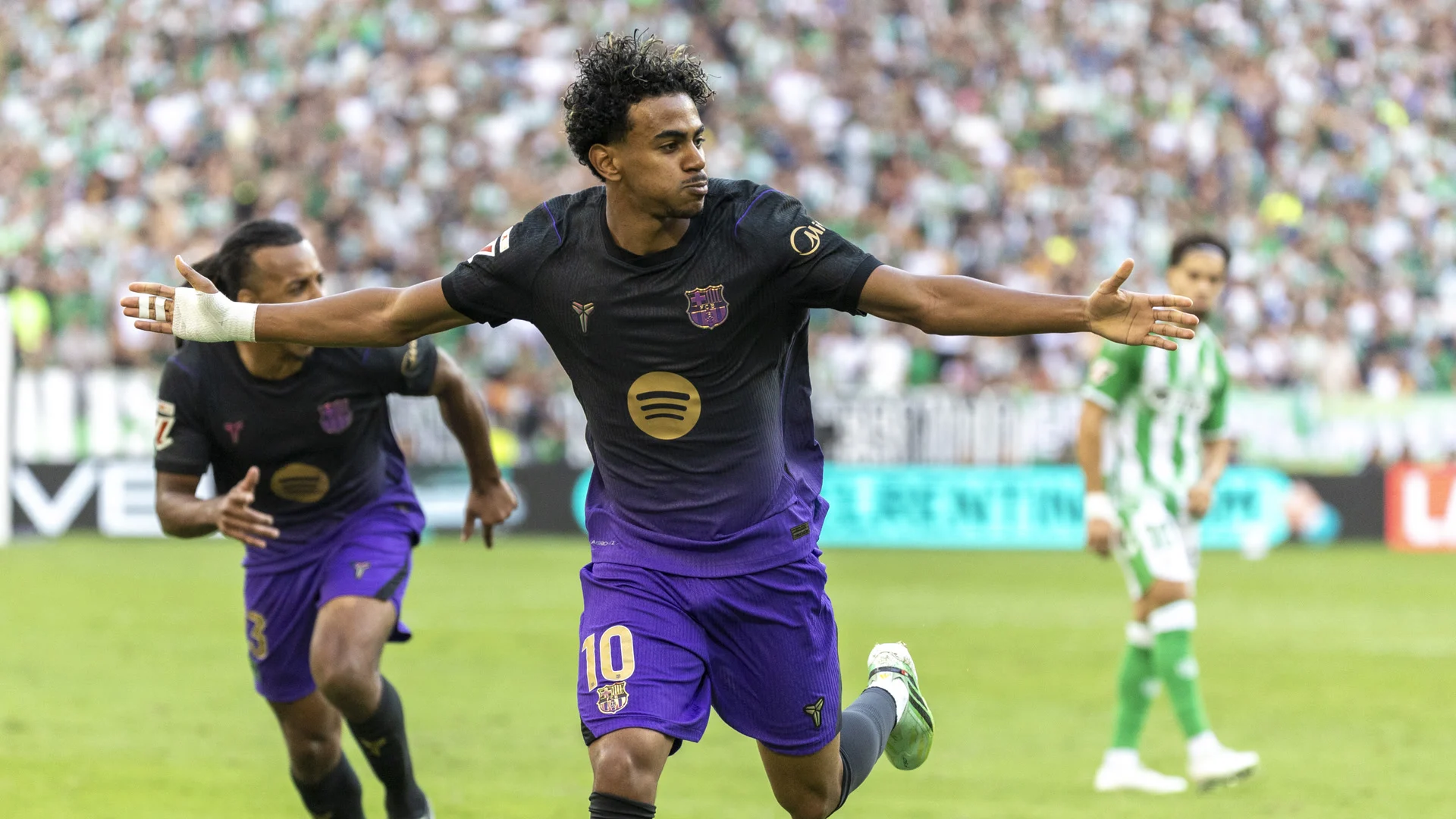 Lamine Yamal, wearing No 10 in Barcelona's dark purple-and-black away kit, celebrates with his arms outstretched after scoring the opening goal against Real Betis at Estadio La Cartuja, with a team-mate running behind him. Photo: J.A. Sirvent/Mundo Deportivo
