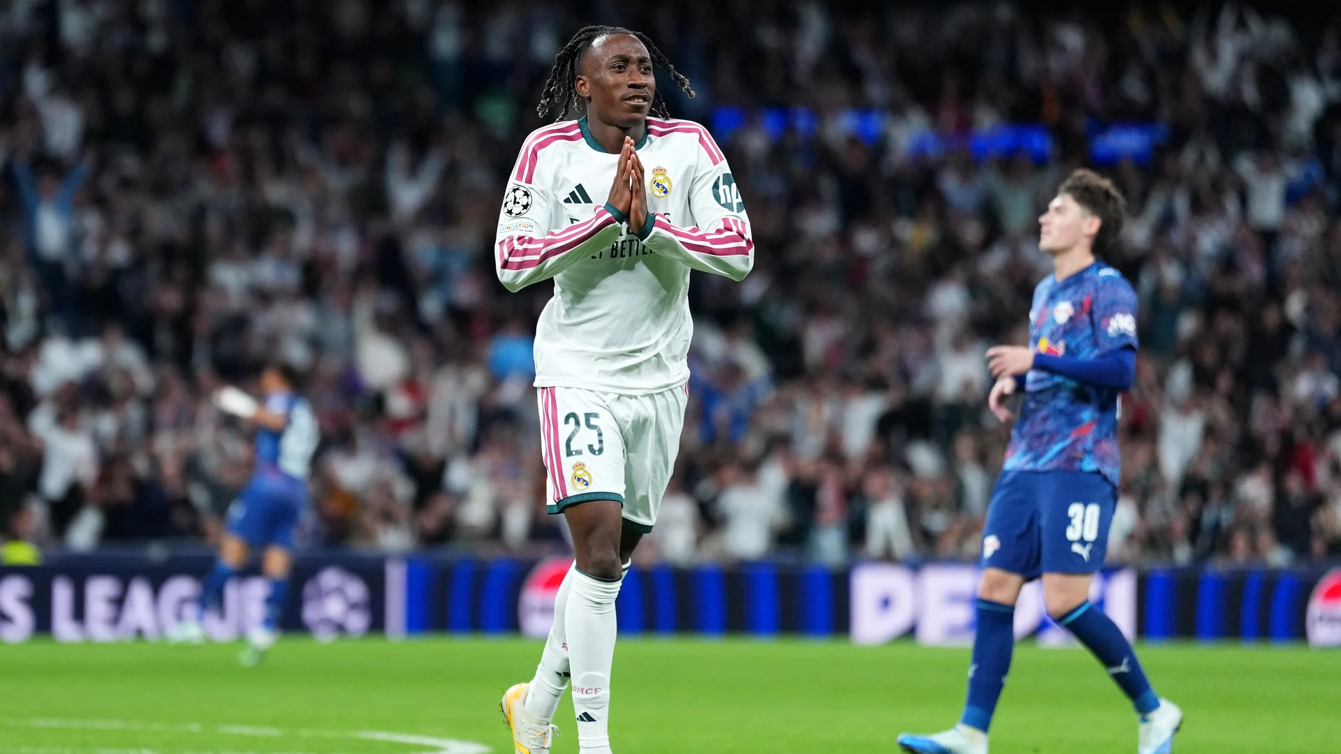 Yan Diomande, in Real Madrid's white home kit with pink trim and number 25 on his shorts, presses his hands together after scoring his volley against RB Leipzig at the Bernabéu, with Leipzig's Andrija Maksimović (number 30) walking away on the right. Photo: Angel Martinez - UEFA/UEFA via Getty Images