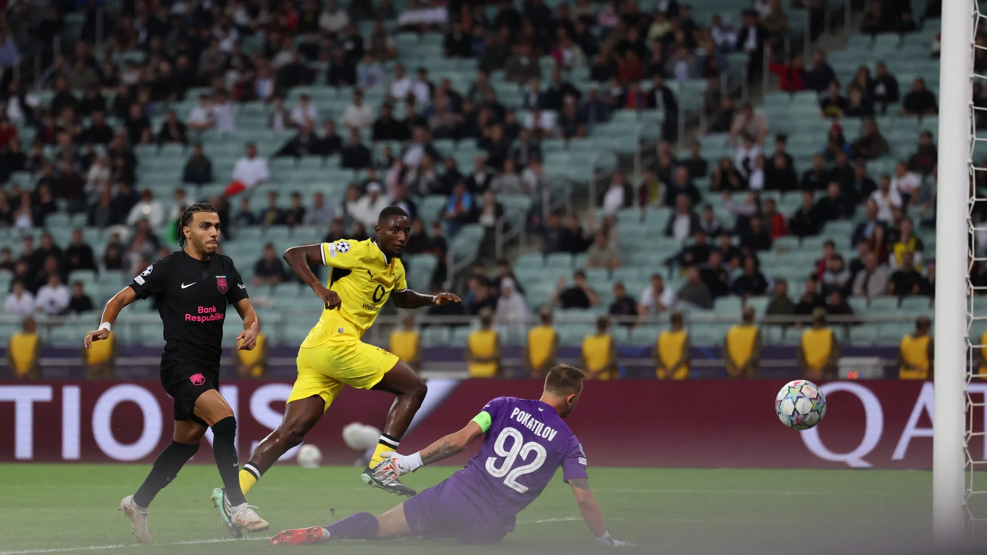 Serhou Guirassy, in Borussia Dortmund's yellow kit, strikes the ball past diving Sabah goalkeeper Stas Pokatilov for the opening goal at the Baku Olympic Stadium, with a Sabah player in black behind him. Photo: Giorgi Arjevanidze / AFP via Getty Images