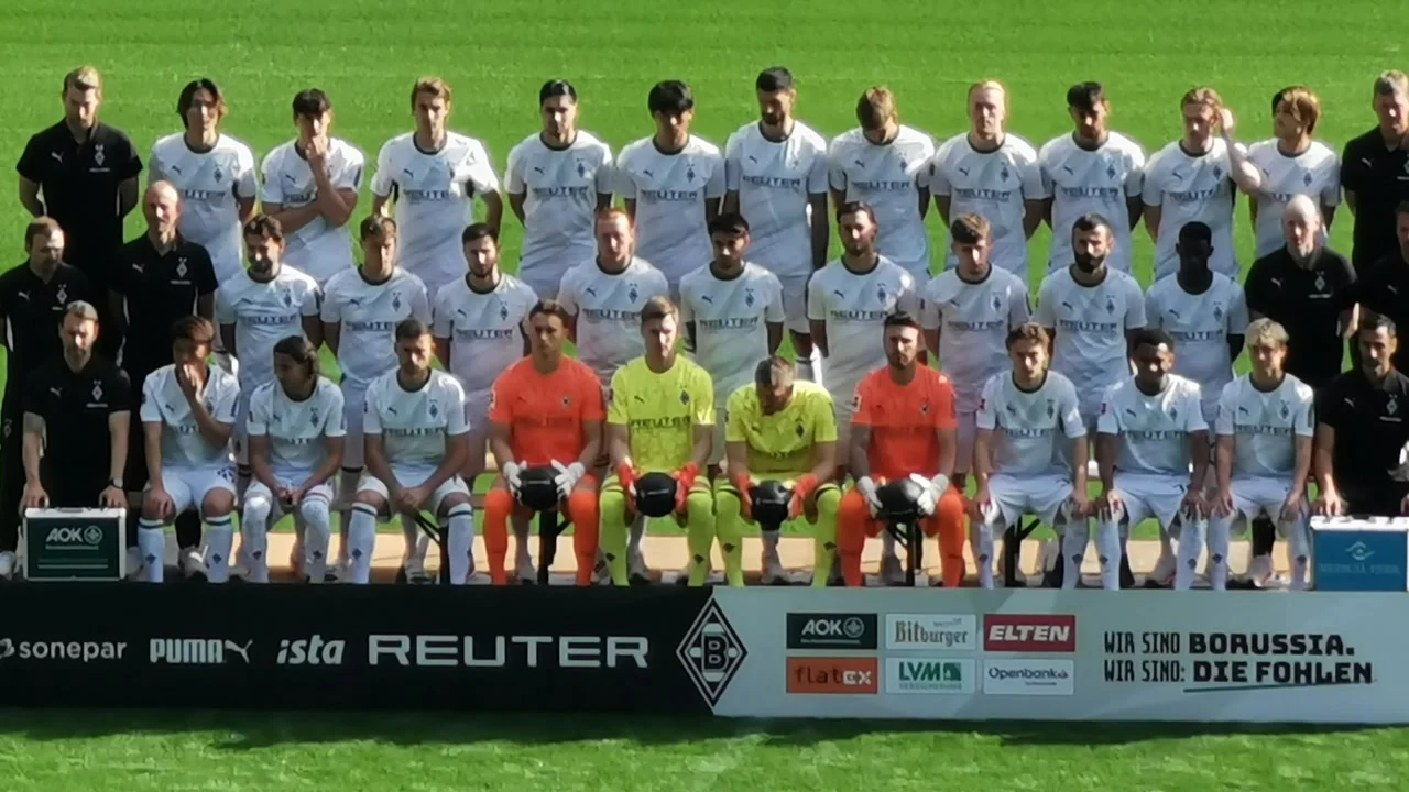 The Borussia Mönchengladbach squad and staff for the 2026-27 season pose for their team photo on a pitch, players in the white home kit and goalkeepers in orange and yellow. Photo: Mozamaniac / Wikimedia Commons, CC BY-SA 4.0