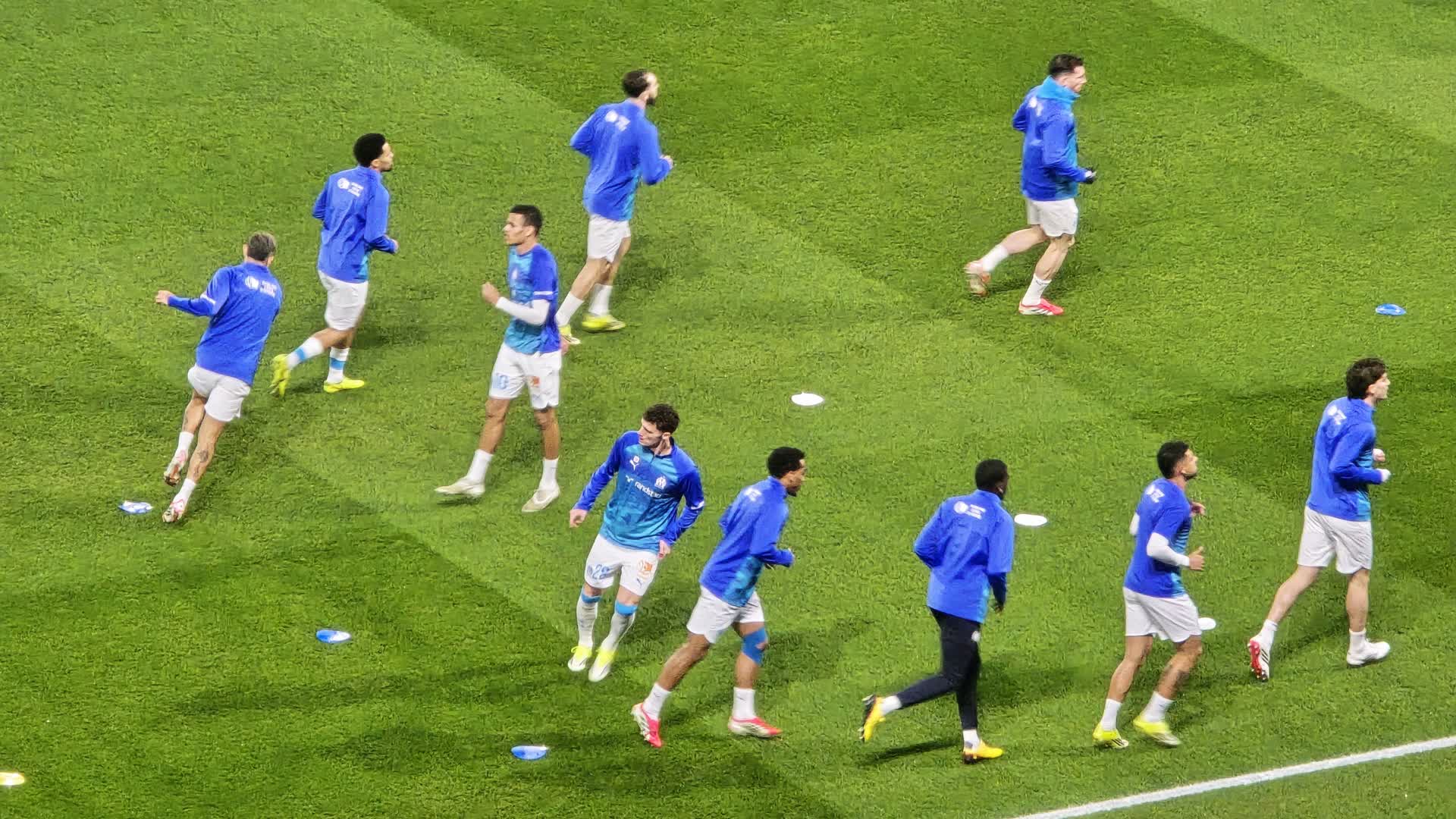 Marseille players jogging in blue training tops during a warm-up on the pitch