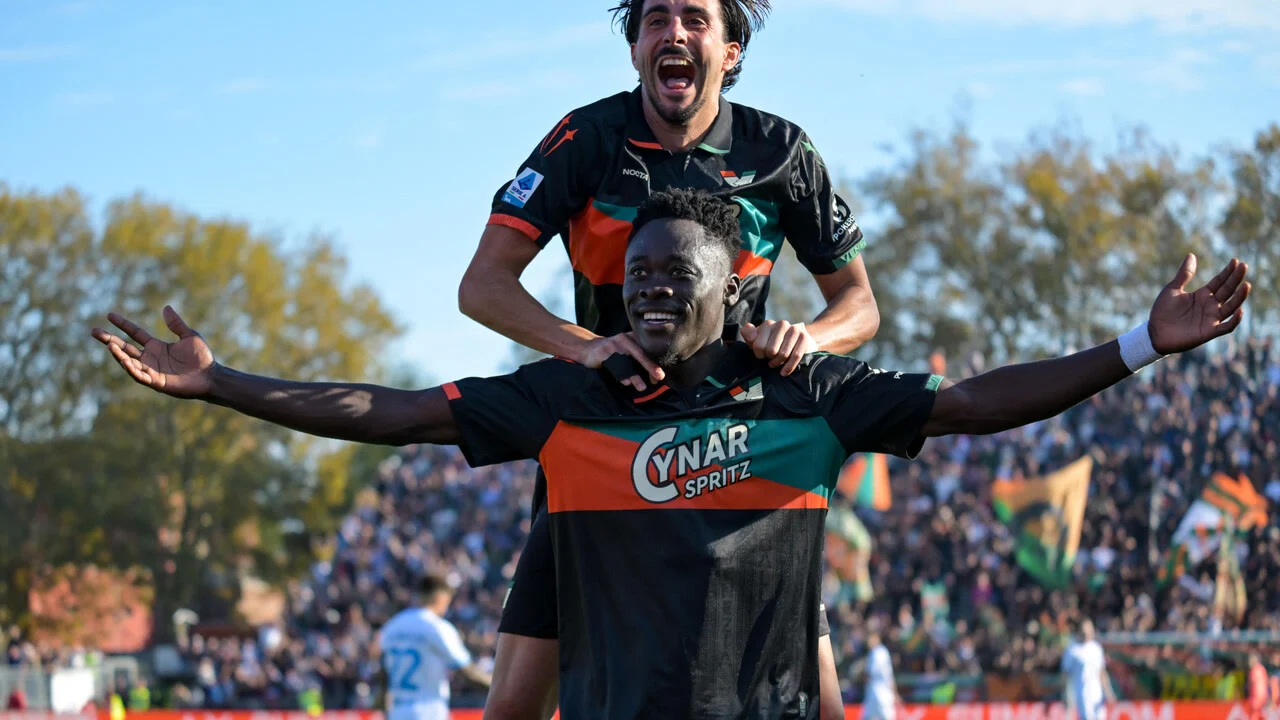 Akor Adams celebrates with his arms outstretched in Venezia's black, orange and green kit as a team-mate jumps on his back after scoring against Napoli at the Stadio Pier Luigi Penzo. Photo: ANSA