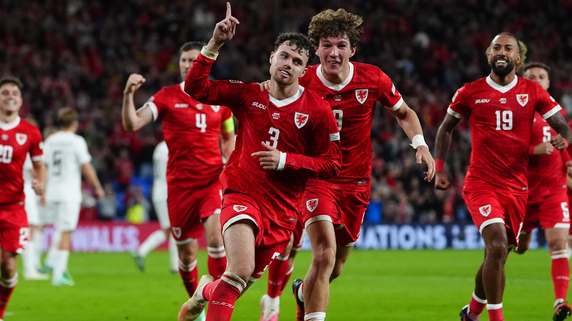 Neco Williams in a Wales national-team shirt celebrating with teammates after scoring against Norway in the Nations League at Cardiff City Stadium